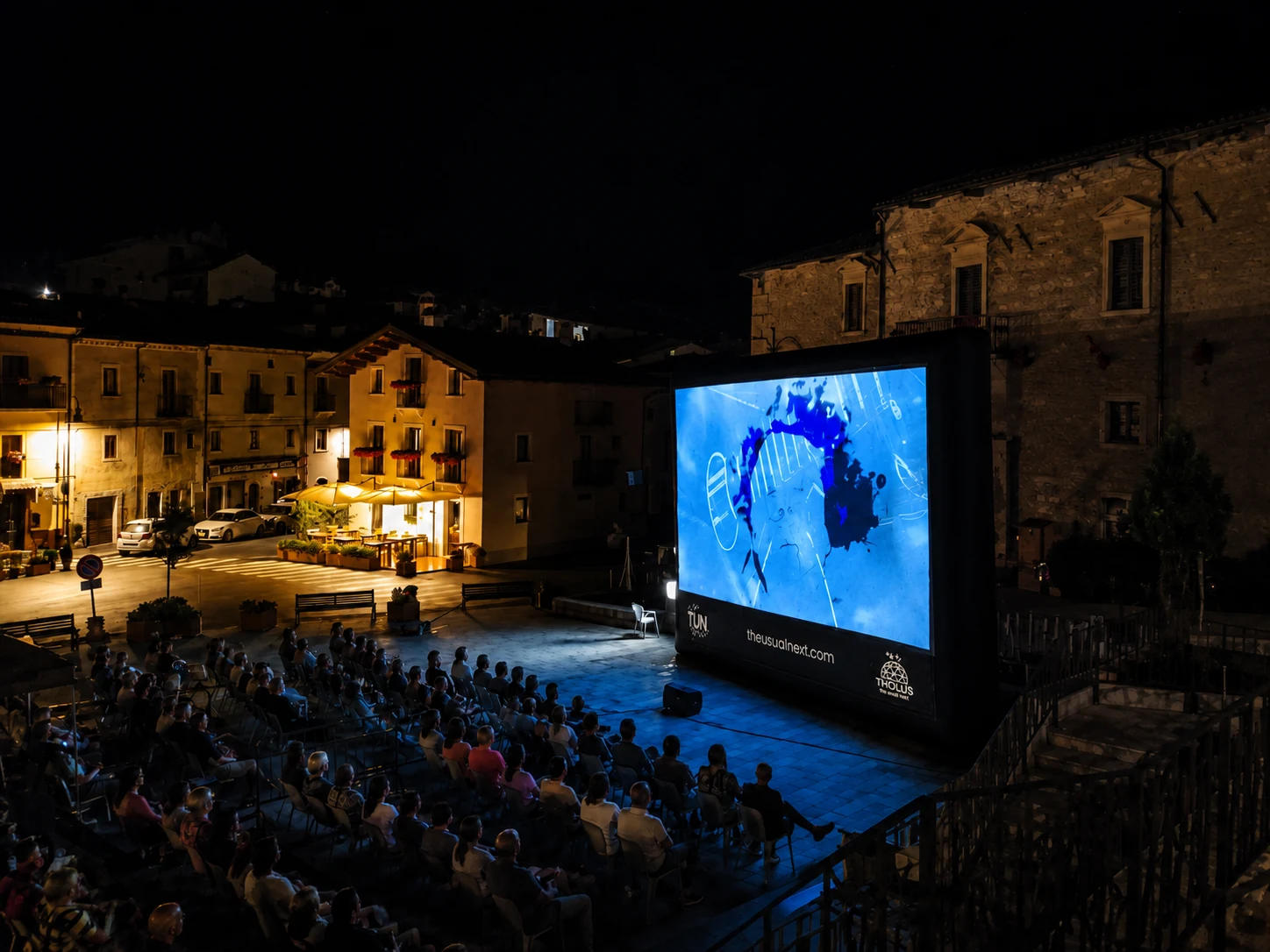 Cinema all’aperto in piazza con schermo gonfiabile e pubblico.